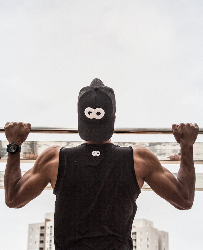 gallery-1 Back view of a man in gym attire doing pull-ups outdoors, demonstrating strength and fitness.